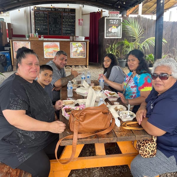 A family of six enjoys burgers and other dishes at an outdoor picnic table at Taro Hut.
