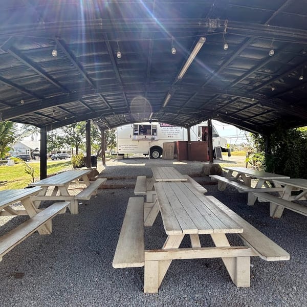 Outdoor covered seating area with multiple picnic tables and the Taro Hut food truck in the background.