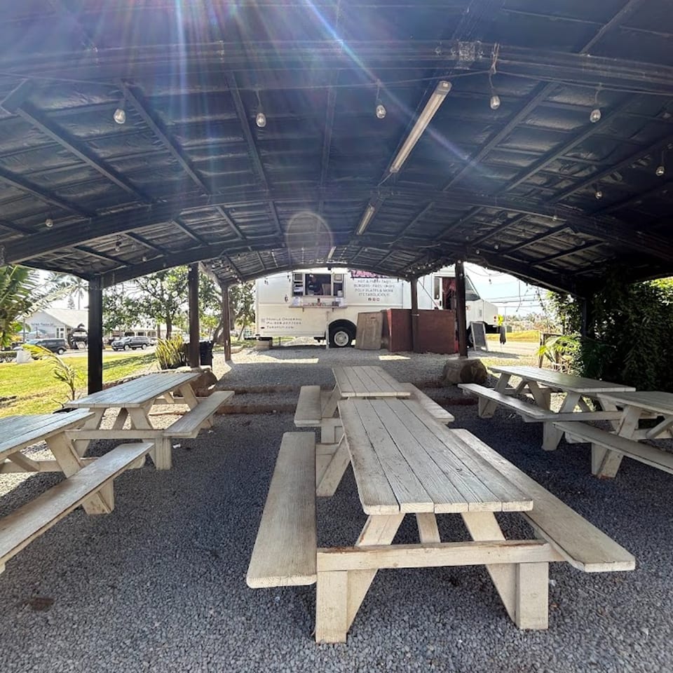 Outdoor covered seating area with multiple picnic tables and the Taro Hut food truck in the background.