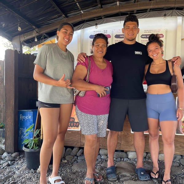 Four smiling people, two women and two men, stand together in front of a Taro Hut food stand.