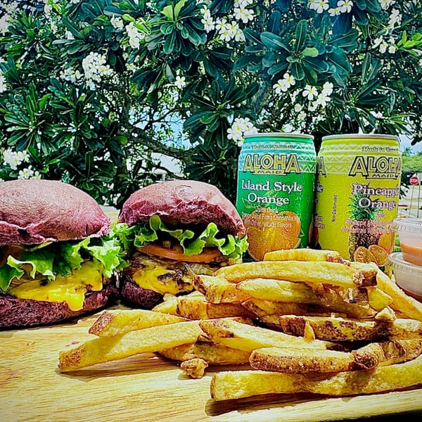 Two Taro Hut burgers with purple buns, fries, and Aloha Maid drinks on a wooden table.