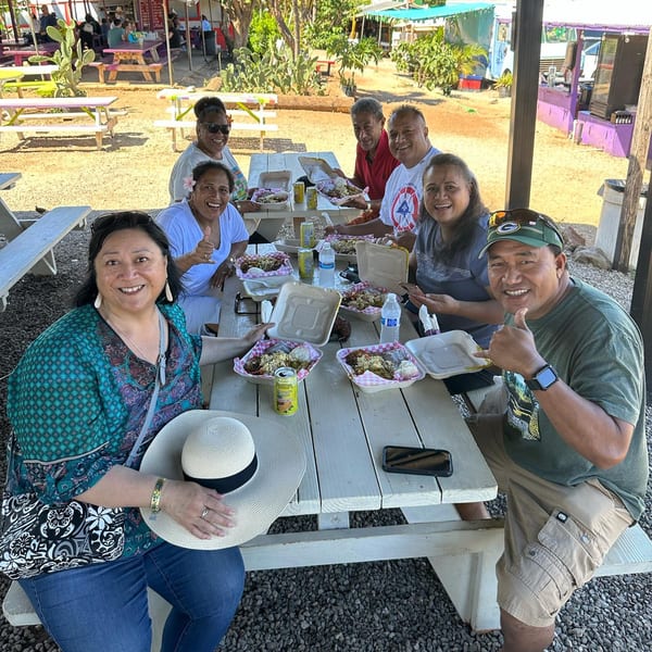 Group of happy customers enjoying meals in takeout containers at outdoor picnic tables at Taro Hut.
