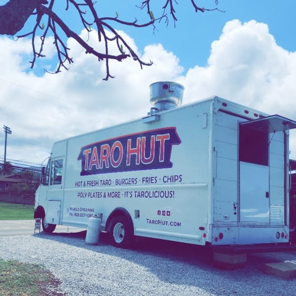 The Taro Hut food truck, white with a blue and red logo, parked on a gravel lot.