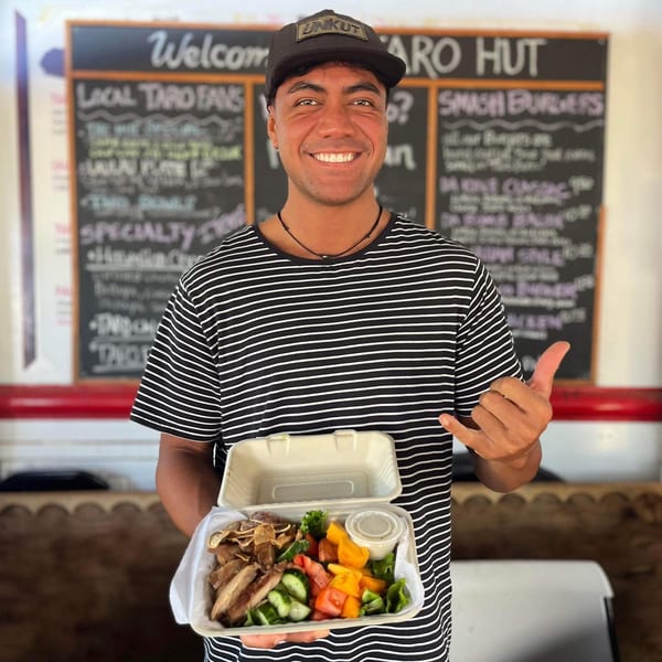 Smiling man in a striped shirt holding an open takeout container with food from Taro Hut.