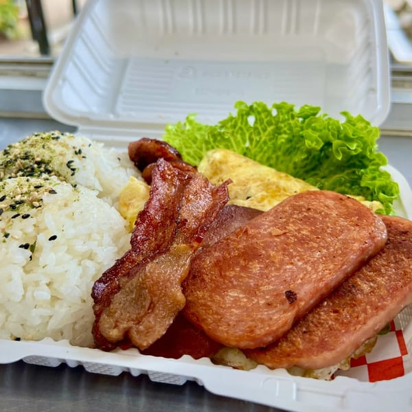 A Taro Hut takeout container with rice, spam, bacon, scrambled eggs, and lettuce.