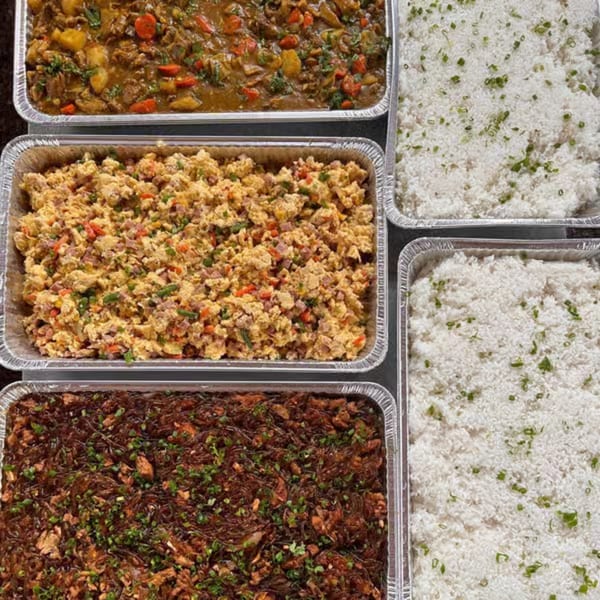 Four catering trays filled with various dishes: curry, scrambled eggs, pancit, and white rice.