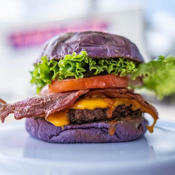 Taro Hut's burger with a purple bun, melted cheese, bacon, lettuce, and tomato.